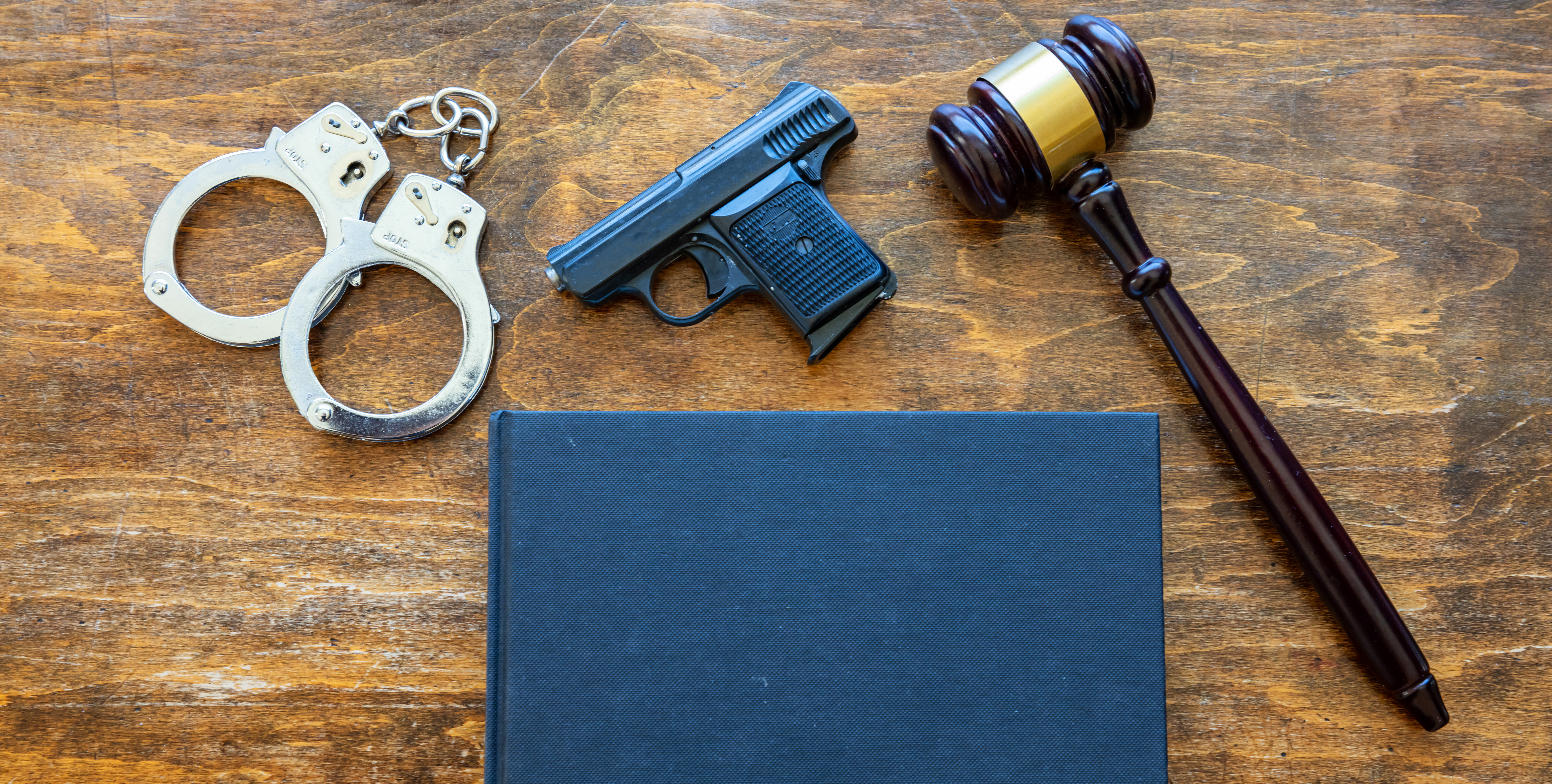 Gavel, handcuffs, and firearm on wood surface representing a gun charge defense checklist